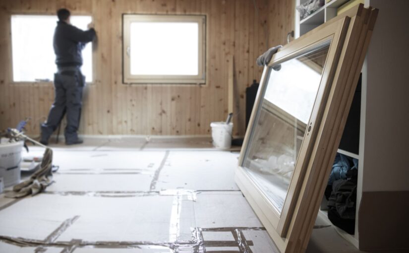 A worker installs new windows in a wooden interior, with energy efficient windows ready for installation in the foreground.